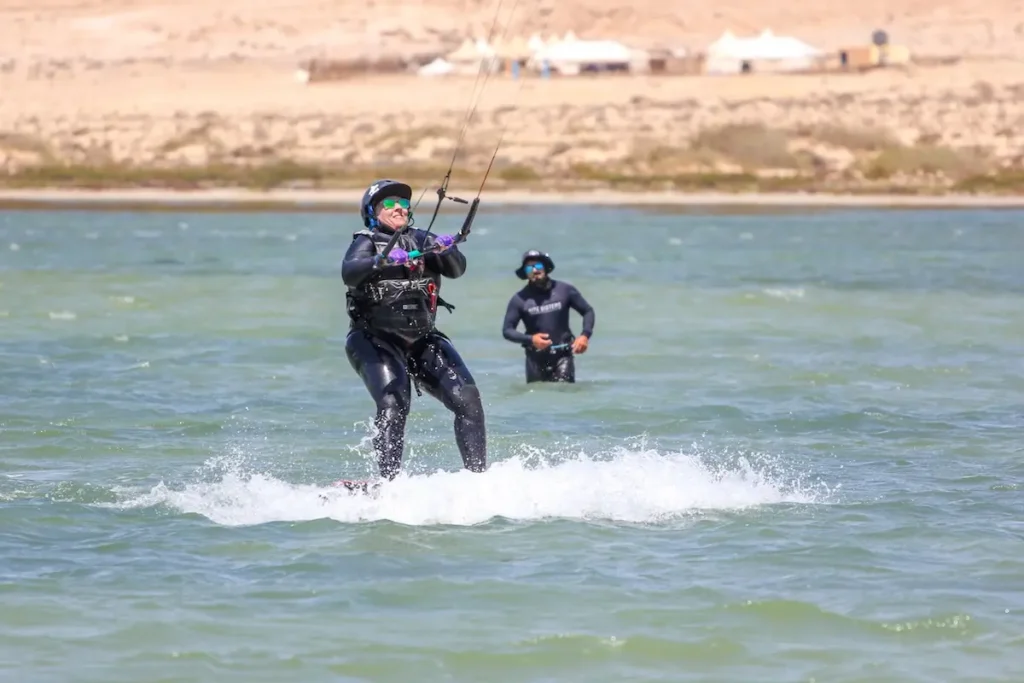 Woman Kitesurfing After 40s on a Beginner-Friendly Lagoon in Morocco - Kite Sisters Woman in her 50s riding a board while kitesurfing on a calm Morocco lagoon, with an instructor watching nearby