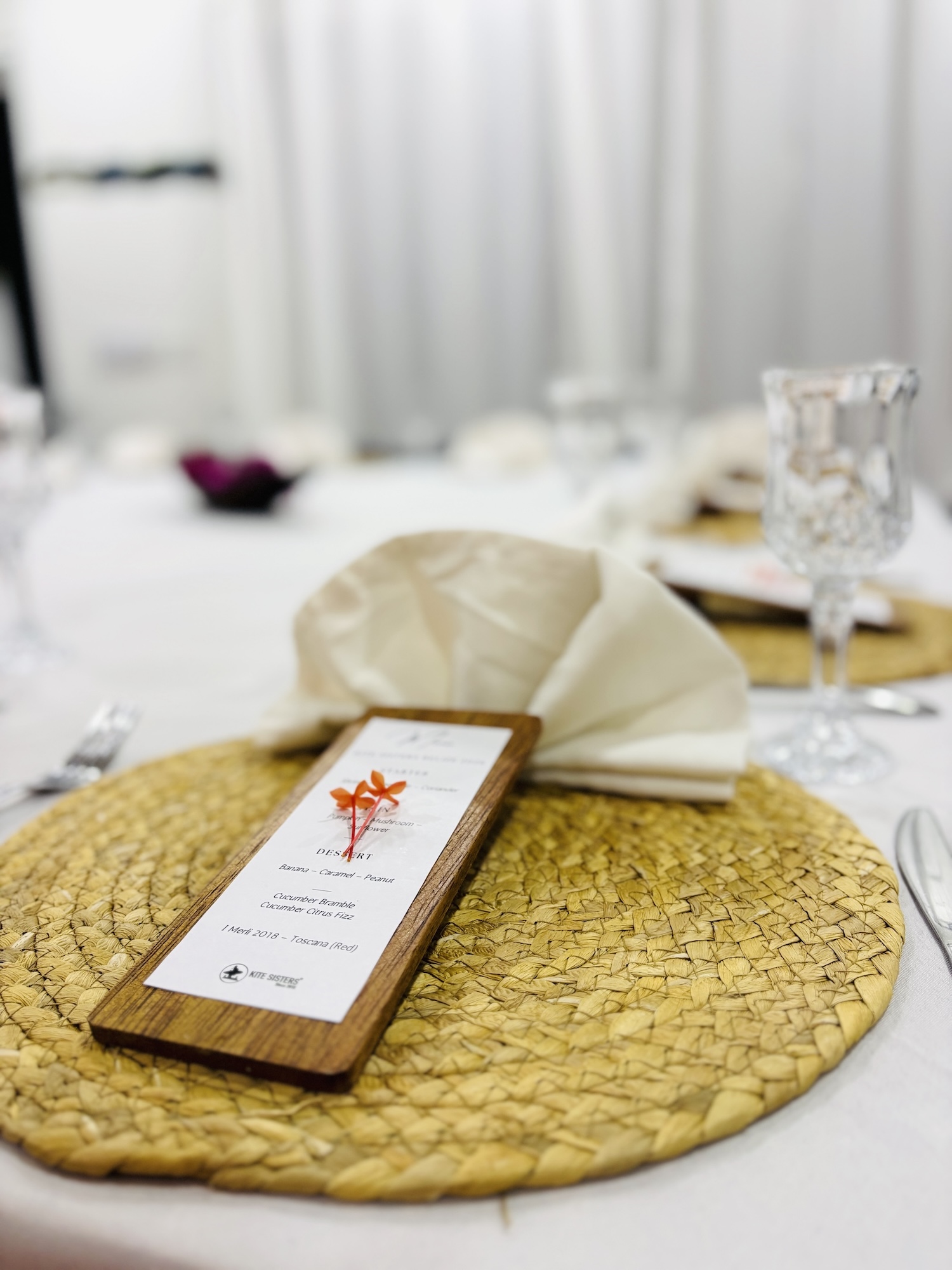 Close-up of a wooden menu card on a woven circular placemat with a folded white napkin at a formal dining table.