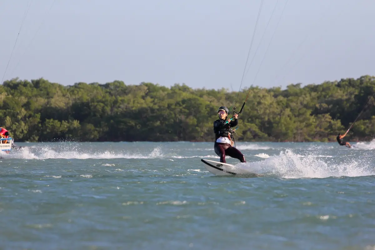 Kite Sisters woman kiteboarding on a Brazil lagoon with a surfboard and mangroves in the background.