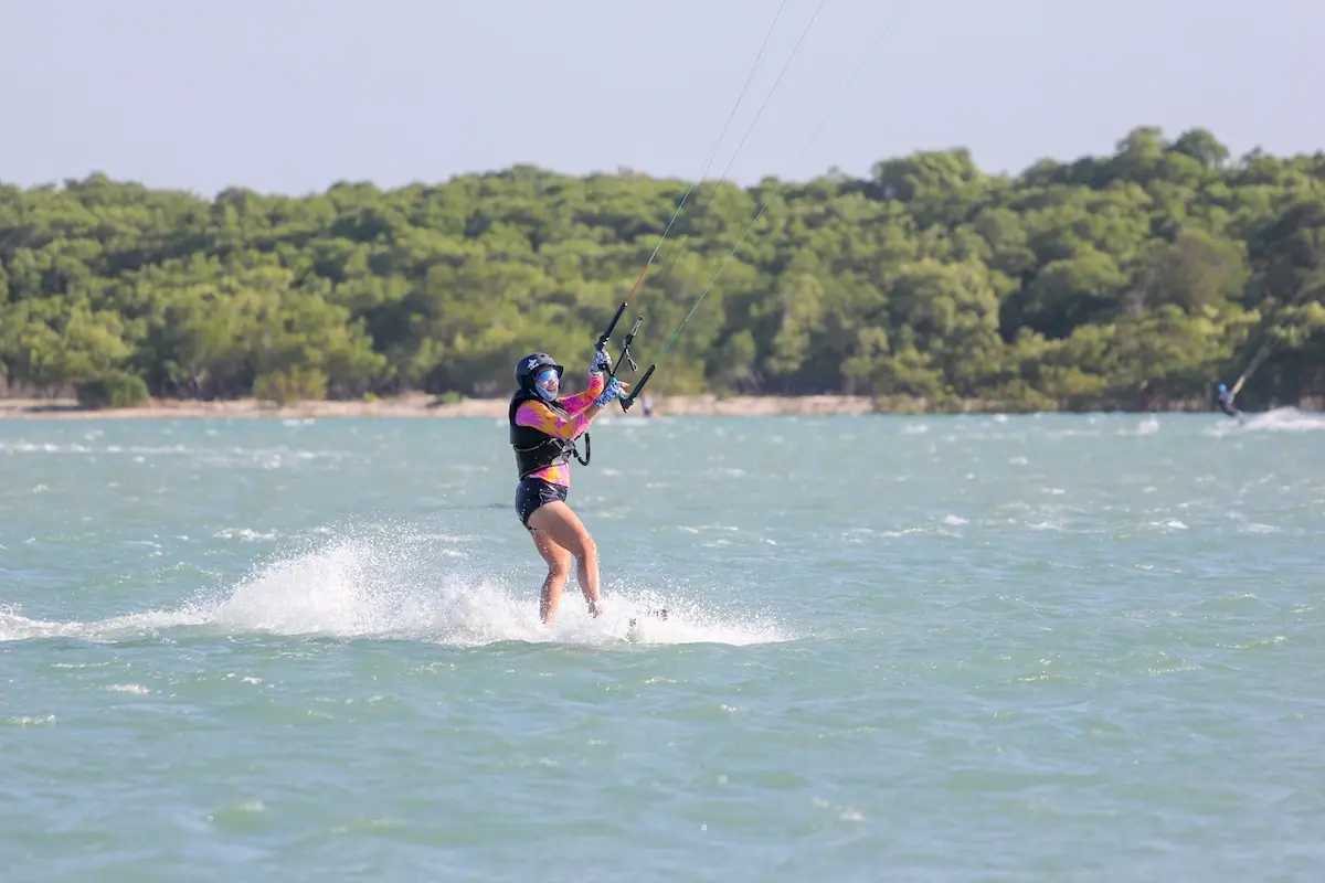Kite Sisters woman kiteboarding on a green lagoon with mangroves in the background at Brazil kiteboarding retreat.