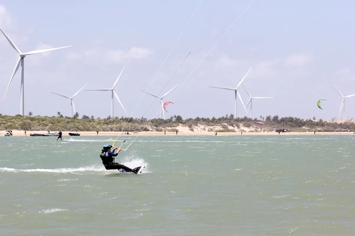 Kite Sisters woman kiteboarding on the Brazil lagoon with large wind turbines in the background.