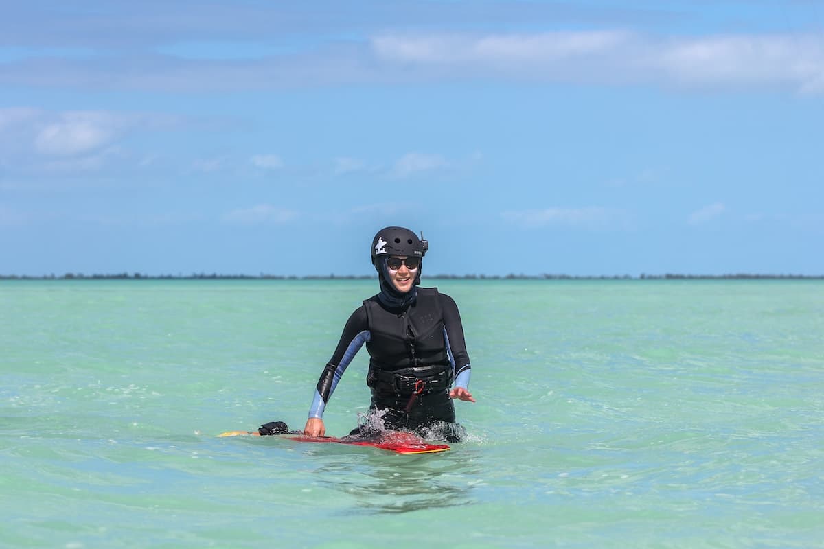 Kite Sisters beginner student smiling with kiteboard in turquoise waist deep water in Belize.
