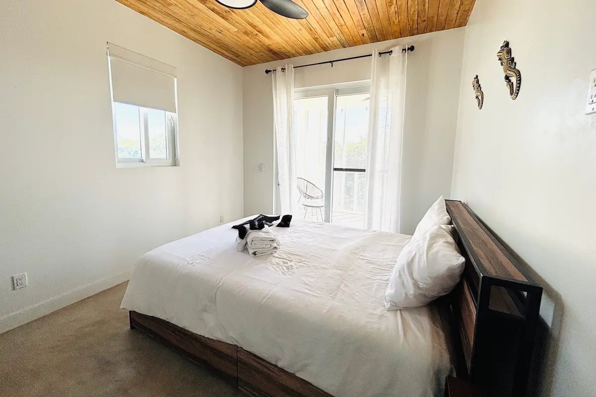 Clean and bright deluxe bedroom with wooden ceiling and private balcony at Kite Sisters Belize retreat.