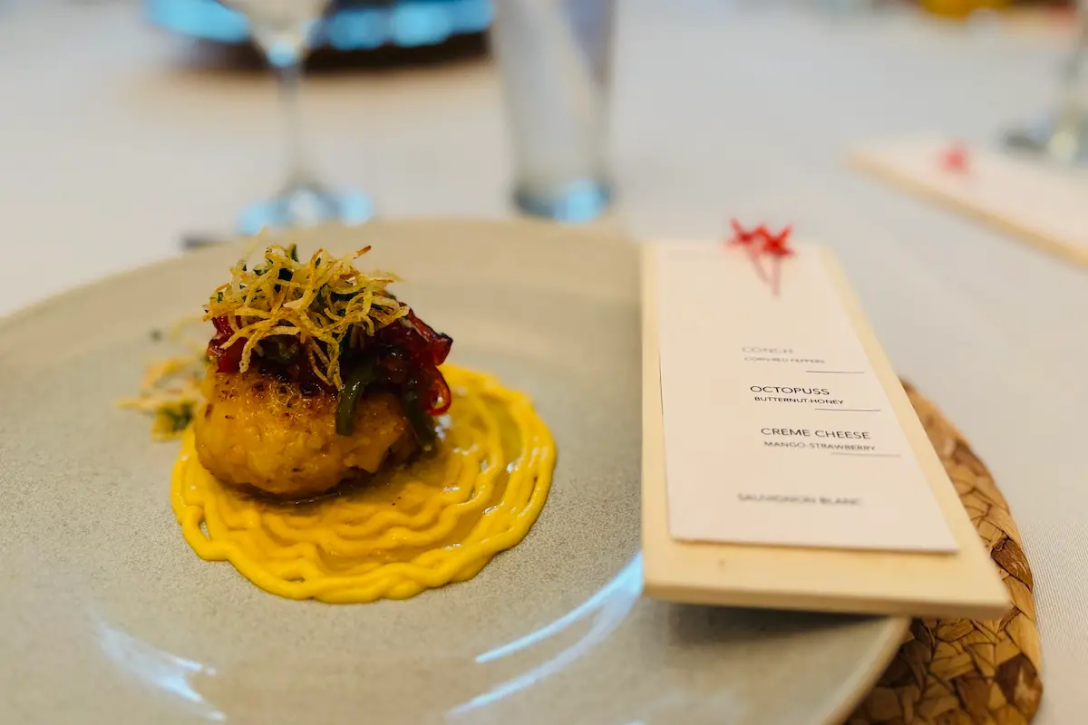 Gourmet conch fritter starter with yellow sauce and tasting menu card at Kite Sisters Belize retreat dining.