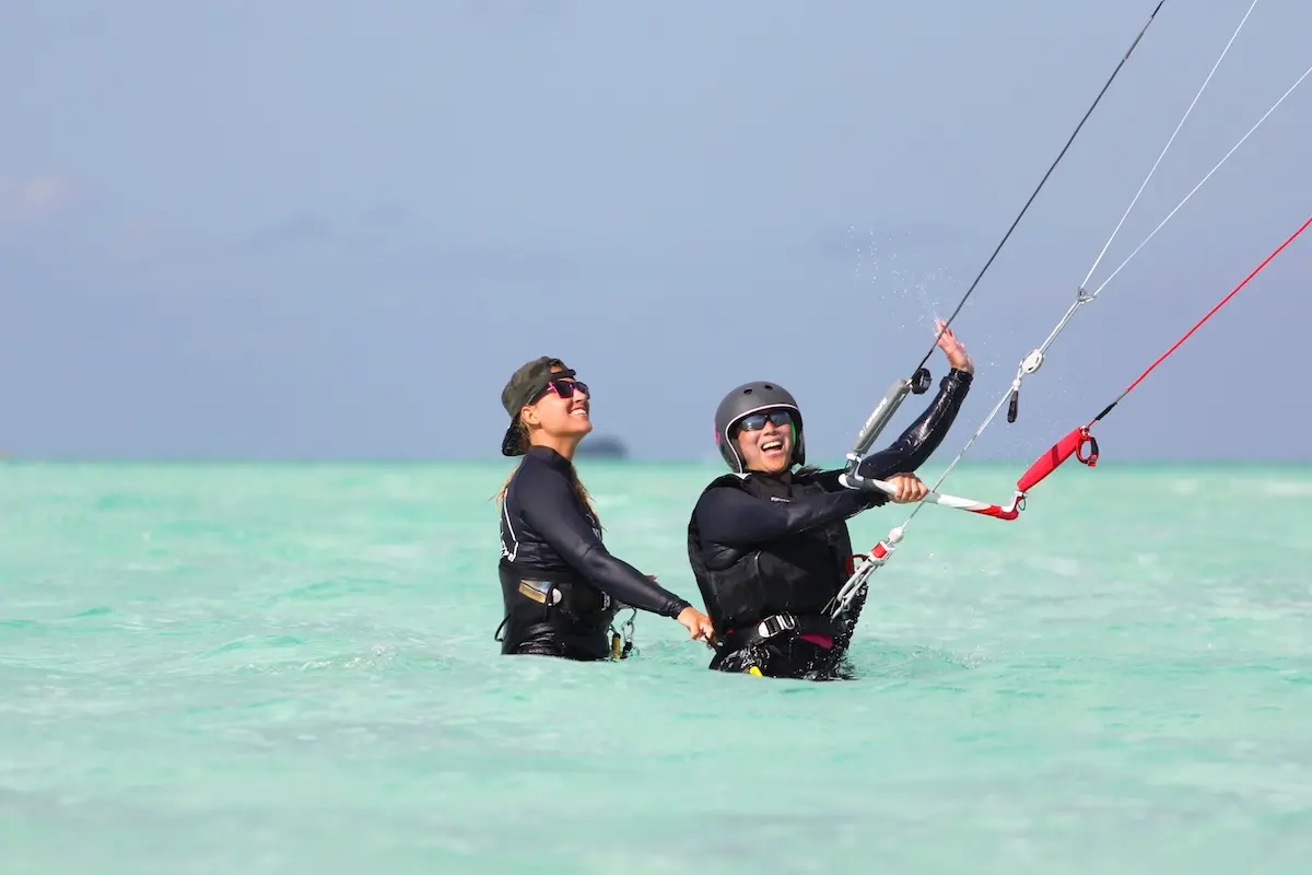 Kite Sisters instructor and student laughing together while practicing kiteboarding in Belize turquoise water.