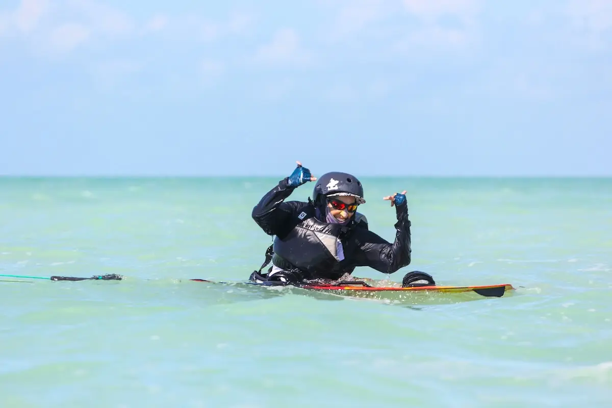 Kite Sisters student celebrating on a kiteboard with thumbs up in turquoise water in Belize.