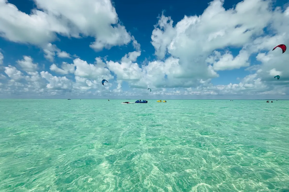 Kite Sisters kitesurf retreat Belize waist deep sandbar with colorful kites flying over turquoise water.