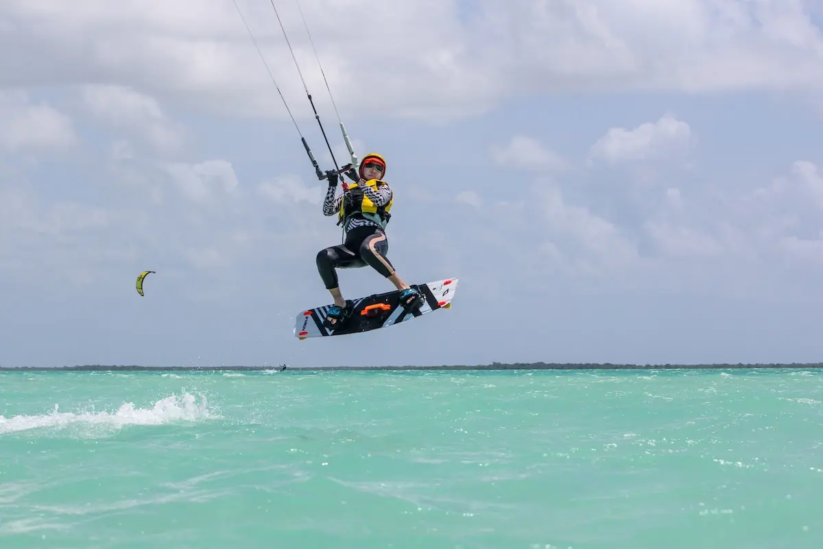 Kite Sisters woman performing a high jump on a kiteboard over turquoise water at Belize kitesurf retreat.