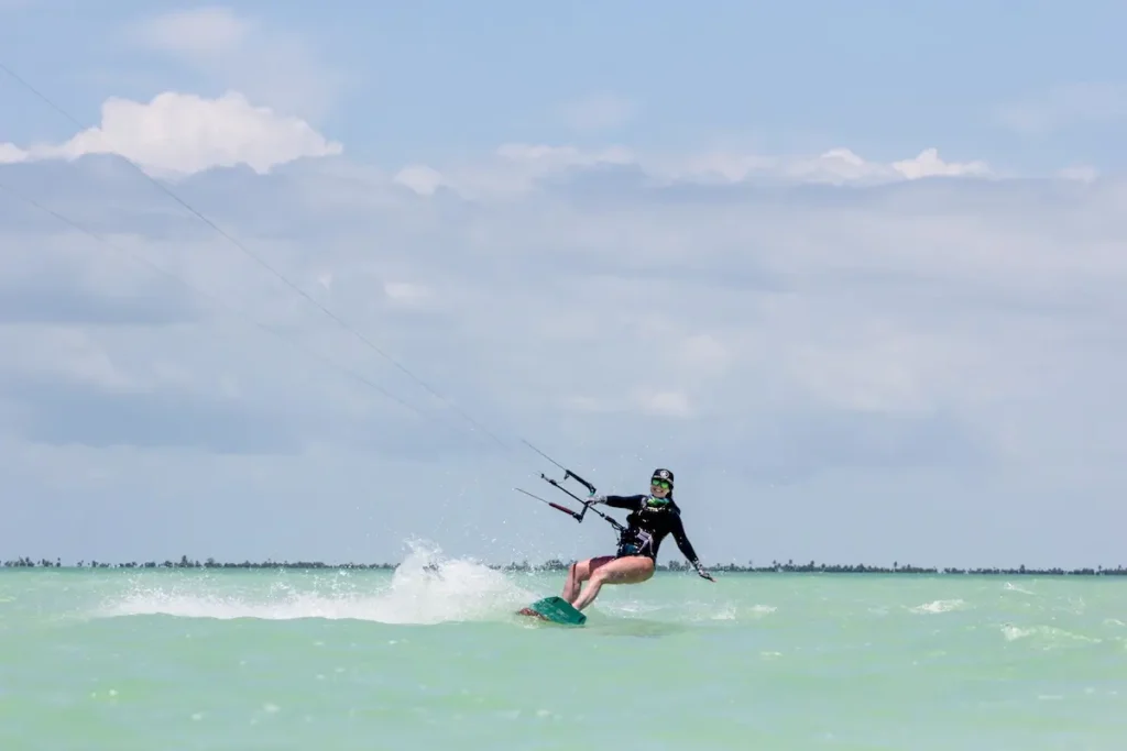 Kite Sisters woman smiling while kiteboarding on turquoise water at Belize kitesurf retreat.