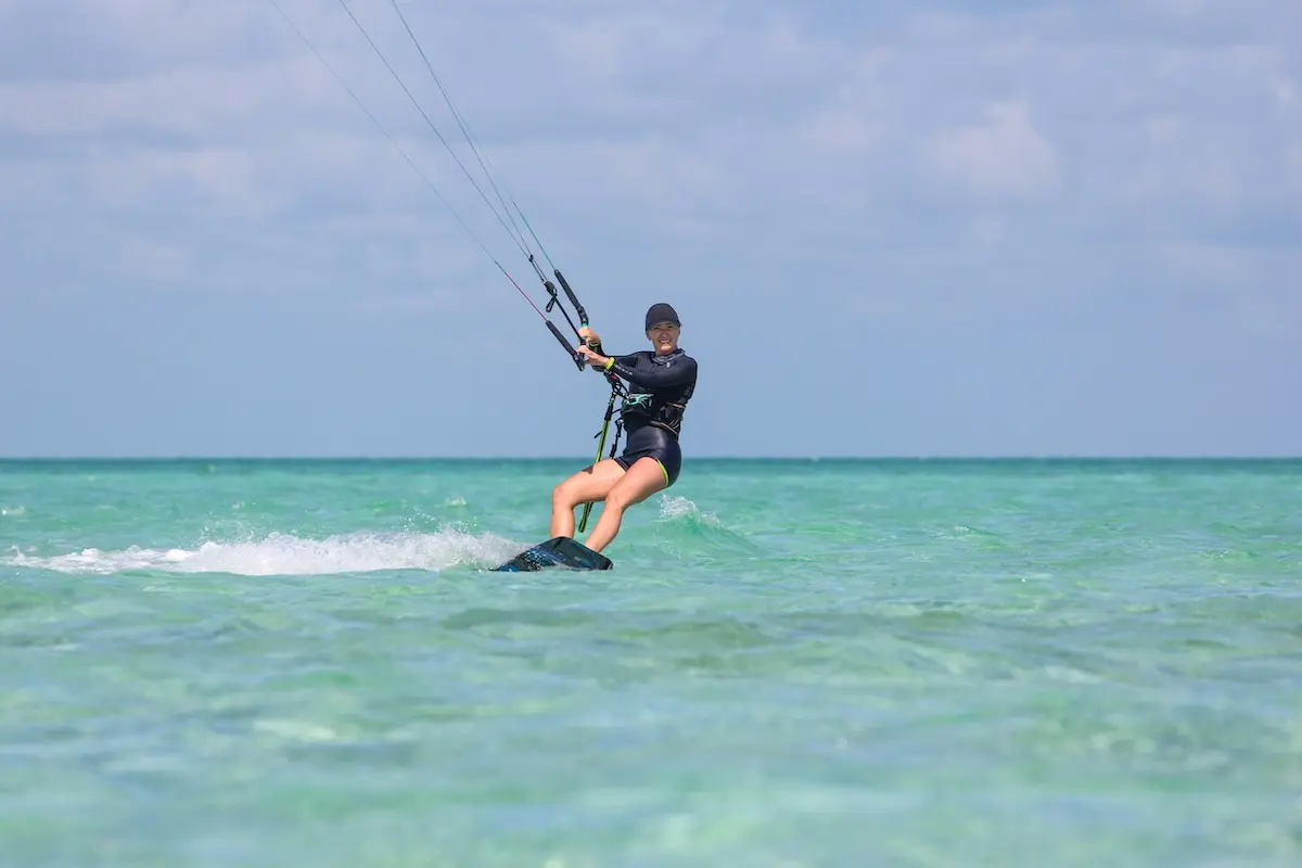 Kite Sisters woman smiling while kiteboarding on flat turquoise water at the Belize kitesurf retreat.