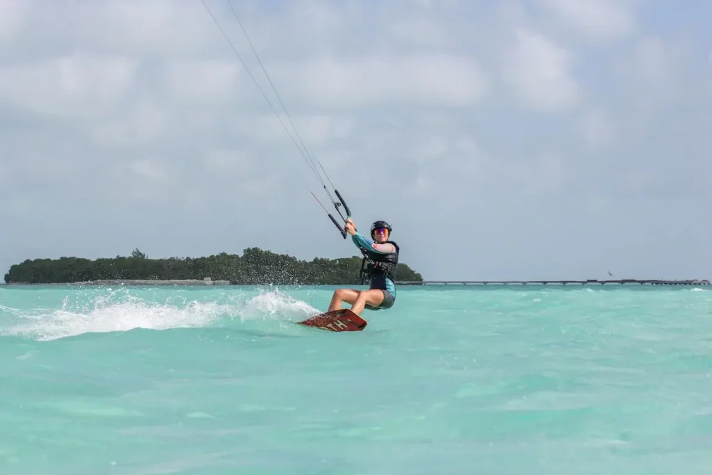 Kite Sisters woman kiteboarding with a tropical island in the background at Belize kitesurf retreat.