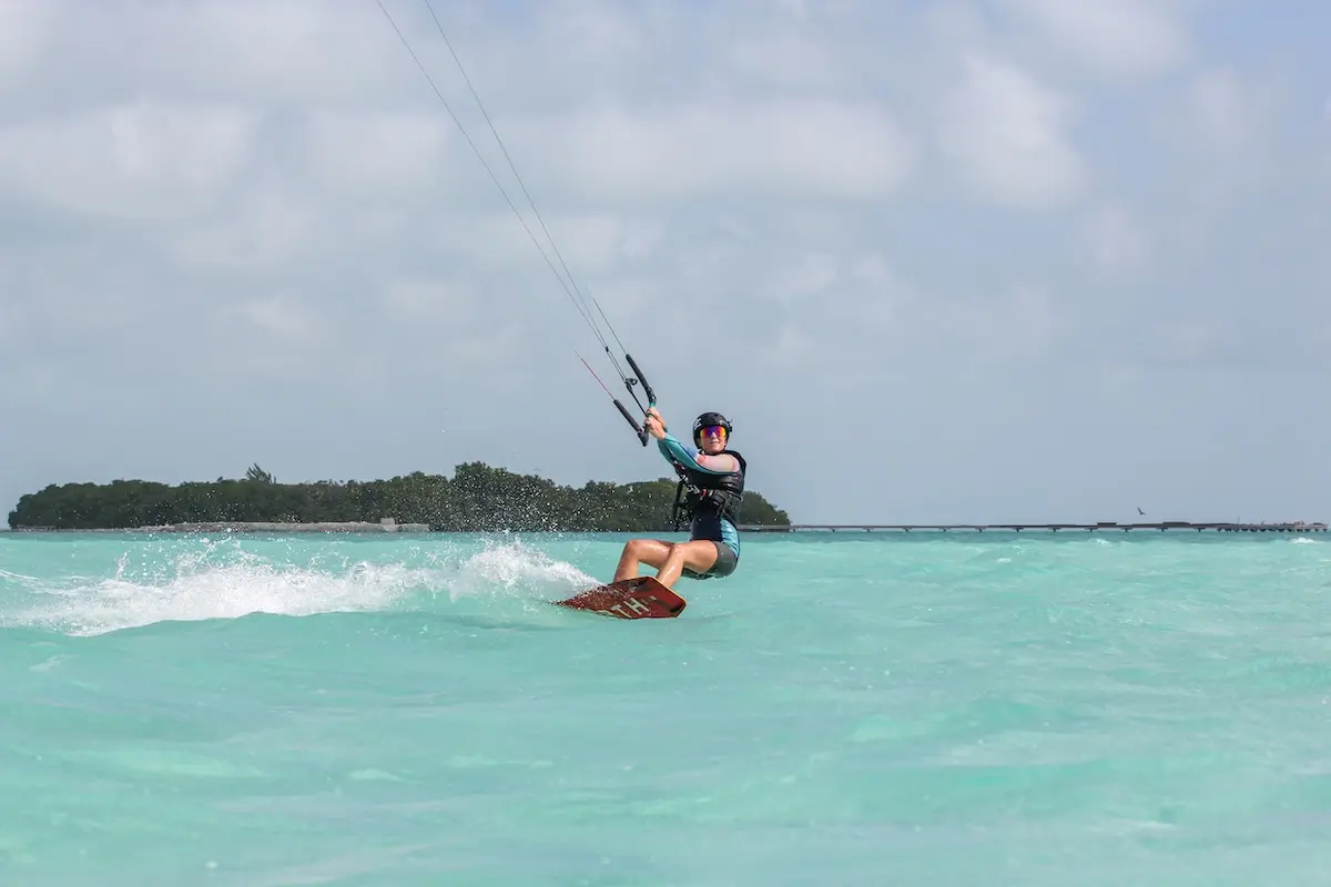 Kite Sisters woman kiteboarding with a tropical island in the background at Belize kitesurf retreat.