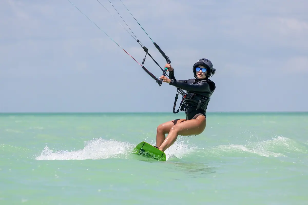 Kite Sisters woman riding a kiteboard in action on turquoise water during Belize kitesurf retreat.