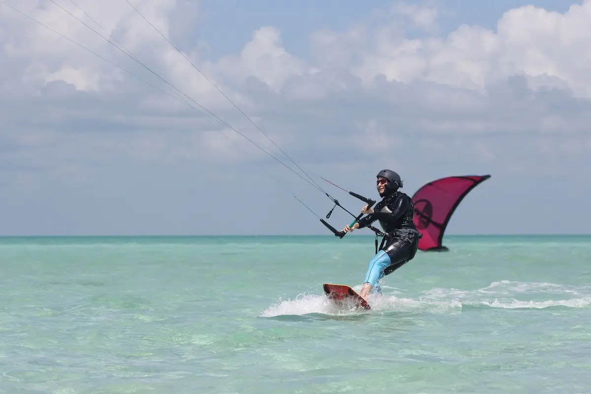 Kite Sisters woman kiteboarding with a pink kite on turquoise water at the Belize kitesurf retreat.