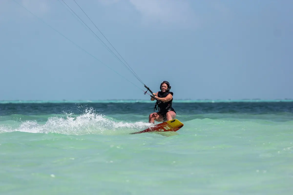 Kite Sisters woman smiling while kiteboarding through waves at the Belize kitesurf retreat.