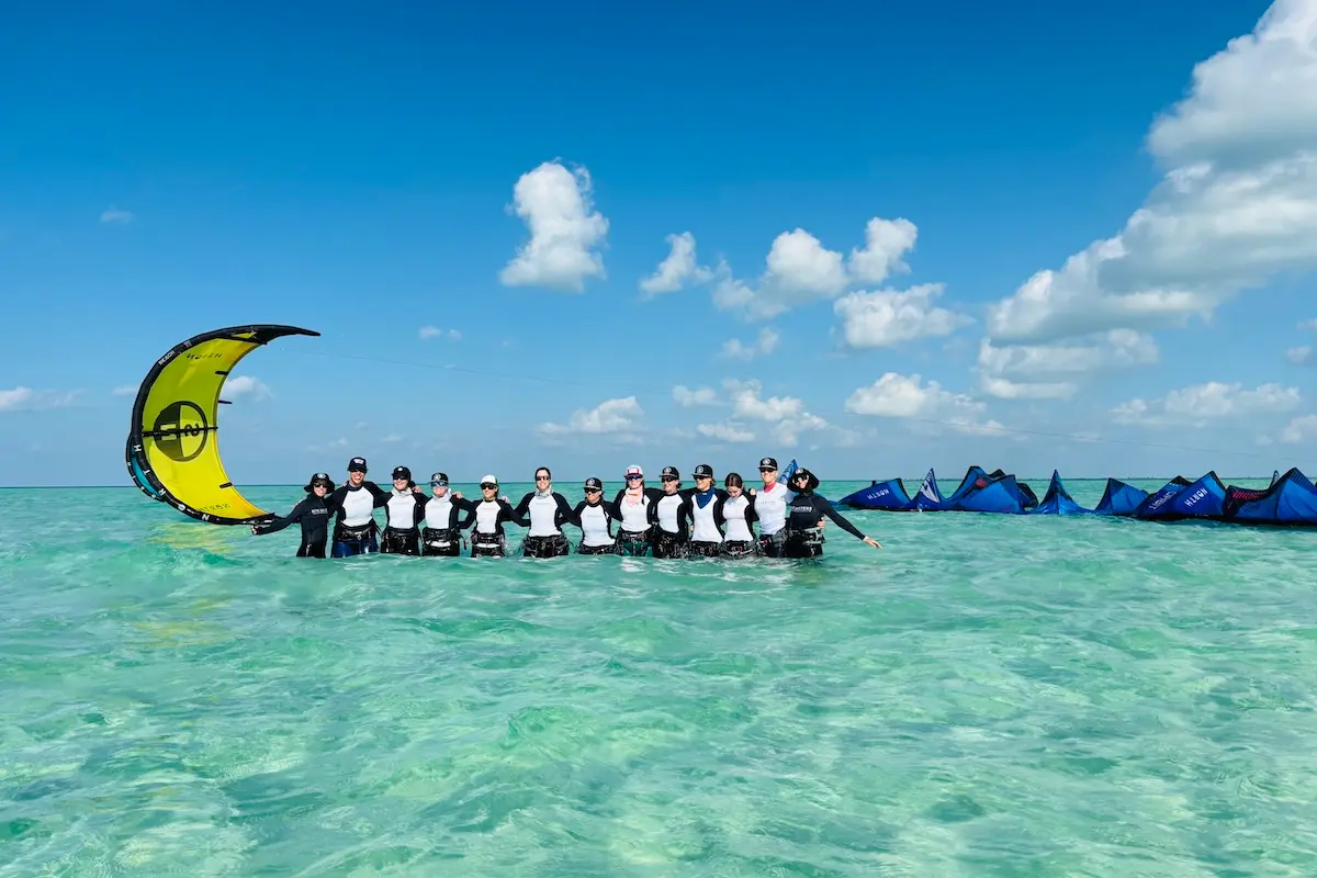 Kite Sisters women group standing together in turquoise sandbar water with kites at Belize kitesurf retreat.