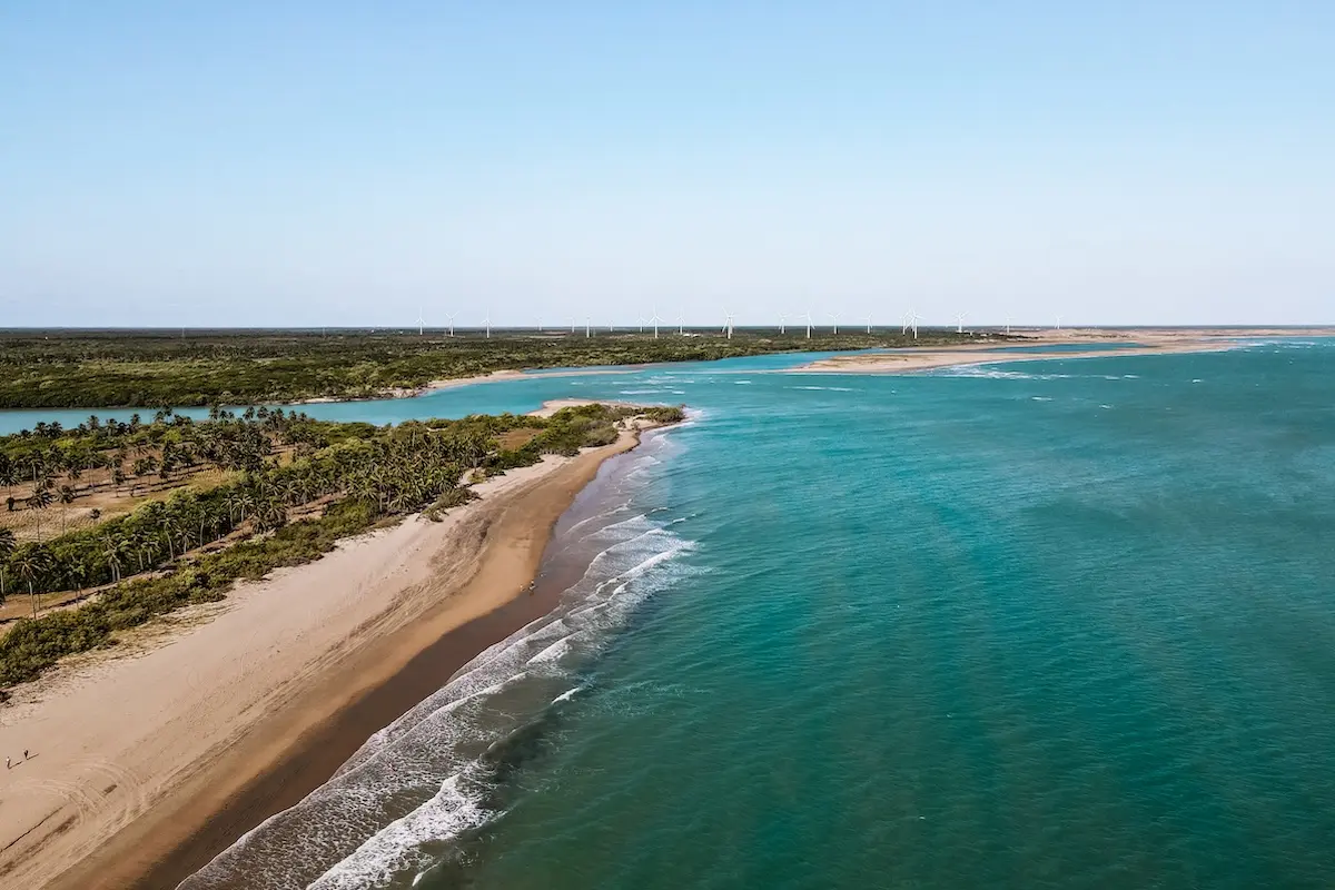 Aerial view of Brazil northeast coastline with turquoise lagoon wind turbines and palm trees at Kite Sisters kitesurf retreat.