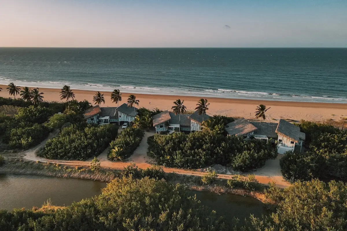 Aerial view of Kite Sisters beachfront villas surrounded by palm trees and ocean at sunset in Brazil.