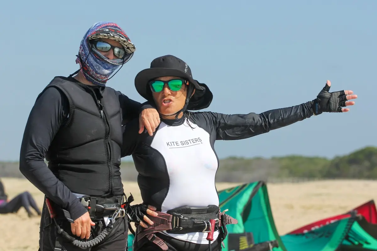 Two women in Kite Sisters gear chatting and laughing on the beach during a kitesurf retreat in Brazil.