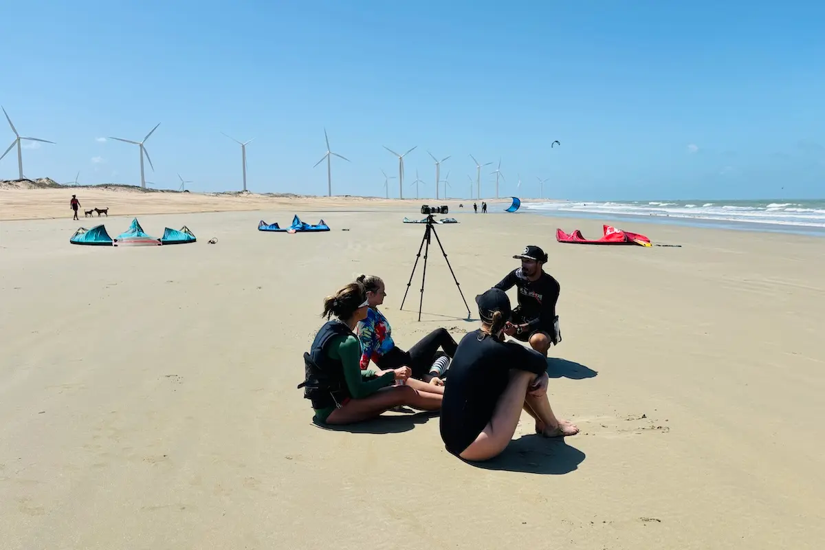 Kite Sisters instructor debriefing students on the beach with wind turbines in the background in Brazil.