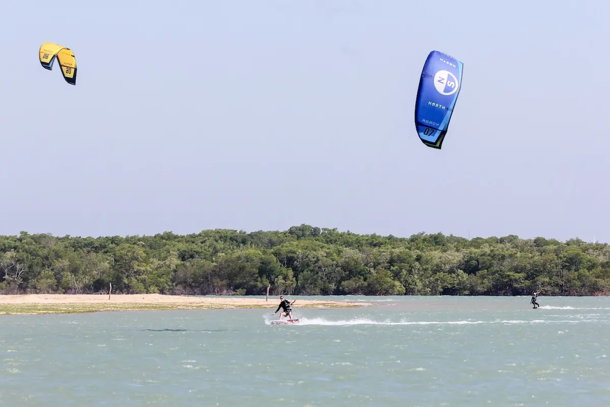 A Kite Sisters rider kiteboarding on a flat water lagoon with colorful kites in Brazil.