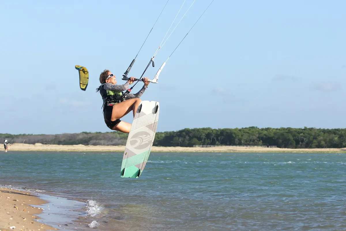 Kite Sisters woman performing a high jump kiteboarding over the Brazil lagoon at kitesurf retreat.