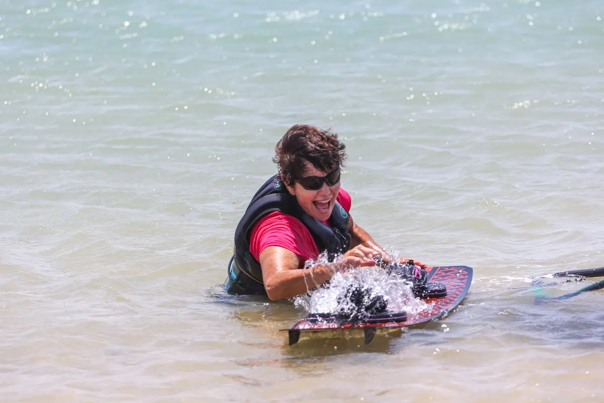 Kite Sisters woman laughing while body dragging on a kiteboard in shallow water at Brazil kitesurf retreat.