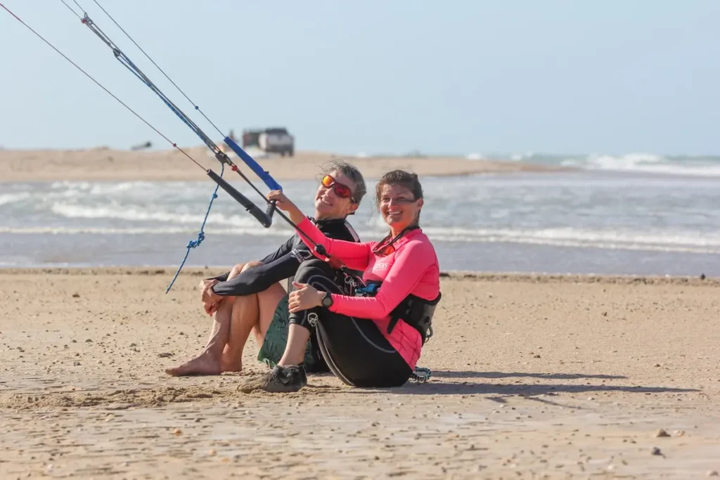 Two Kite Sisters women smiling together on the beach holding a kite bar at Brazil kitesurf retreat.