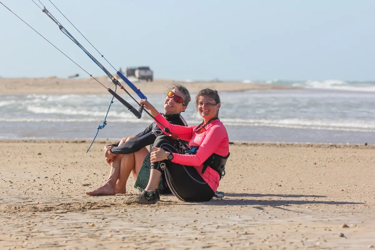 Two Kite Sisters women smiling together on the beach holding a kite bar at Brazil kitesurf retreat.