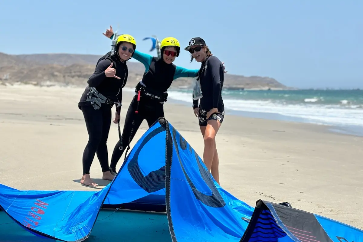 Three women smiling and laughing on the beach with kite gear at Kite Sisters women's kiteboarding camp Peru.