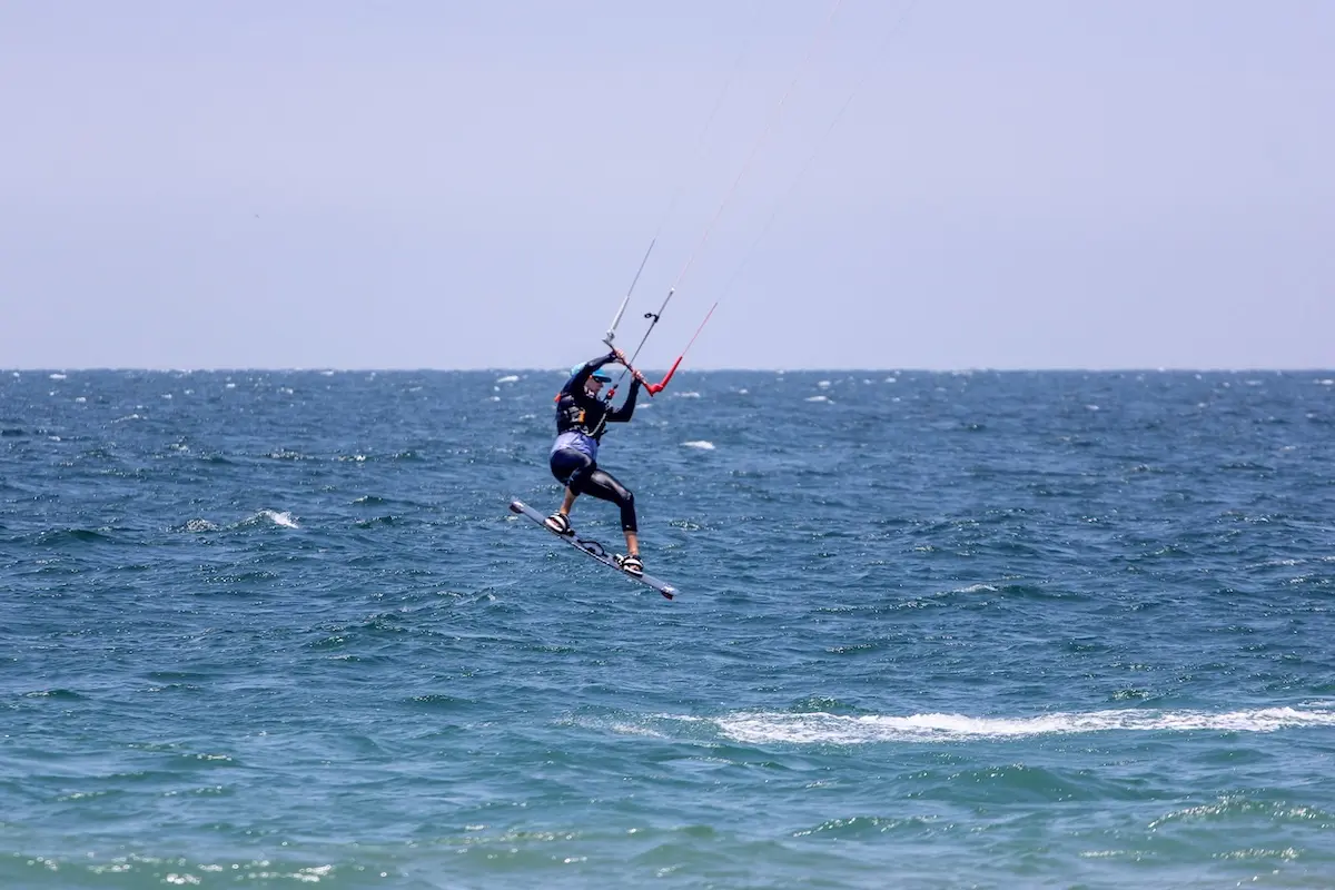 Kitesurfer performing a jump trick above the ocean at Kite Sisters women's kiteboarding camp in Peru.