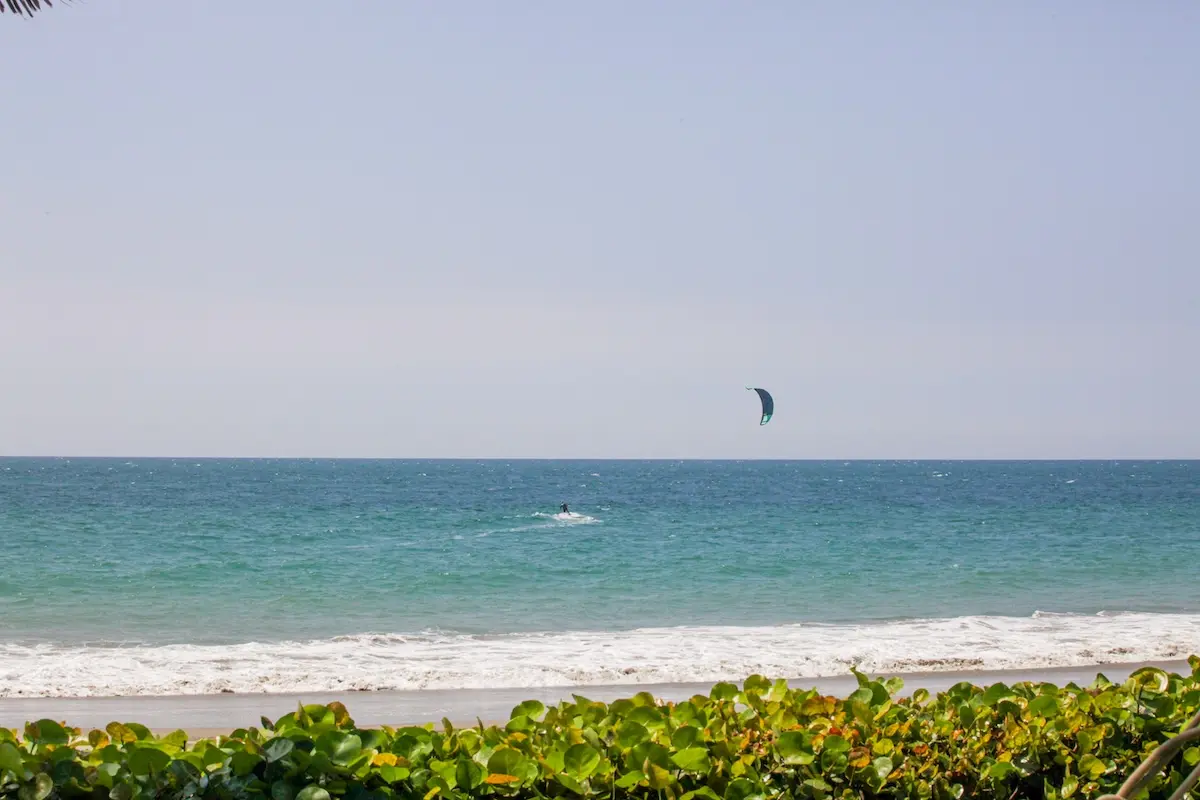 Kitesurfer riding turquoise waves seen from the beach at Kite Sisters women's kiteboarding camp Peru.