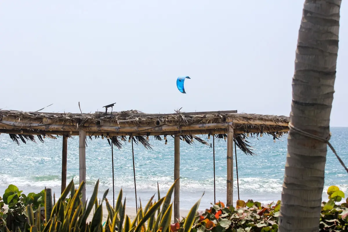 Blue kite flying above the ocean seen through a rustic palapa at Kite Sisters women's kiteboarding camp Peru.