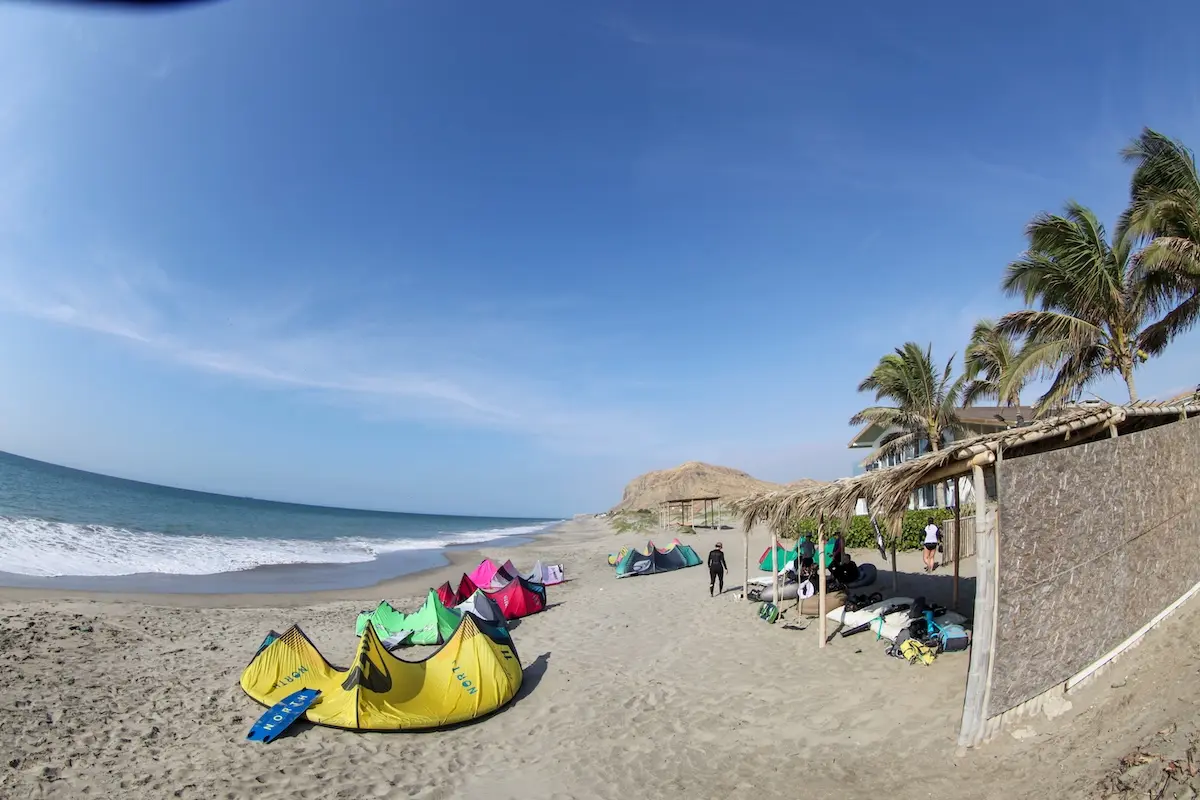 Colorful kites laid out on the beach with palm trees and mountains at Kite Sisters women's kiteboarding camp Peru.