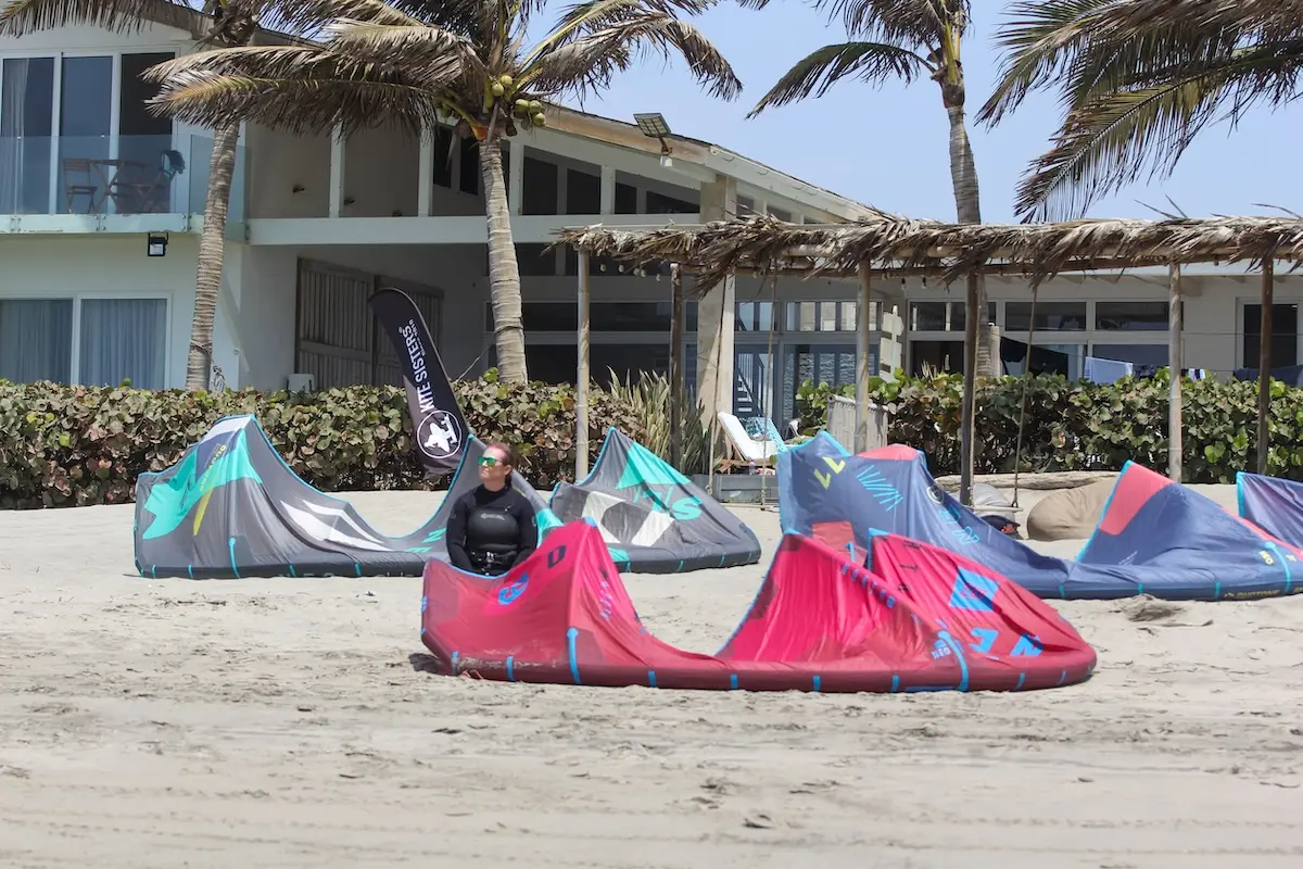 Multiple kites laid out on the beach with the Kite Sisters flag and beachfront villa in the background in Peru.