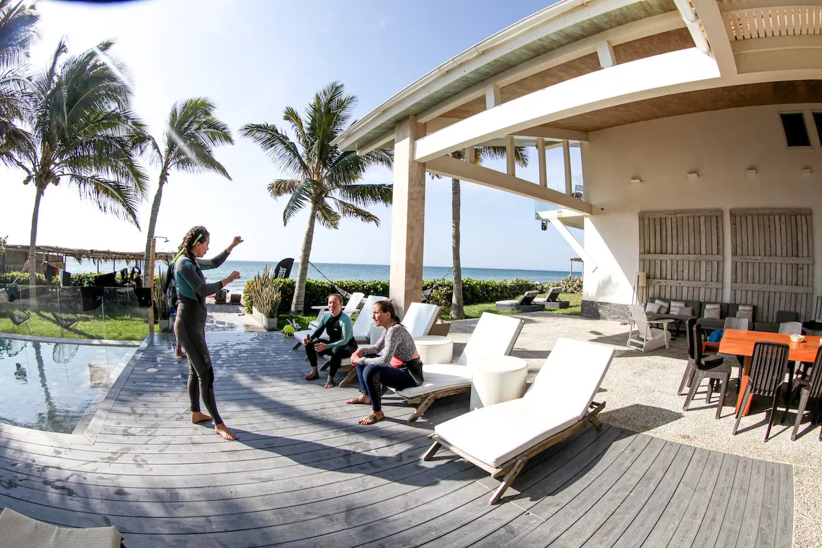 Three women in wetsuits chatting about kiteboarding technique by the pool at Kite Sisters women's camp Peru.
