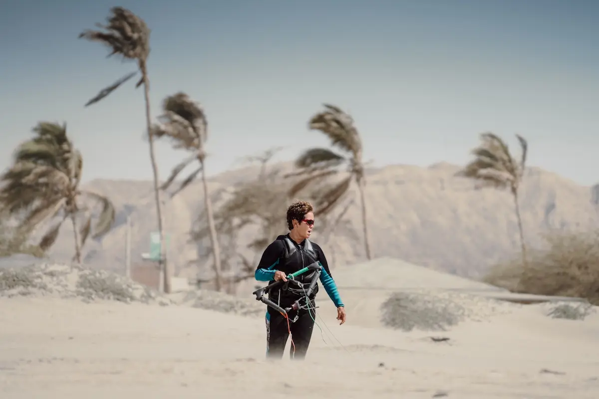 Woman walking on a windy desert beach with kite bar and palm trees bending in the wind in North Shore Peru.