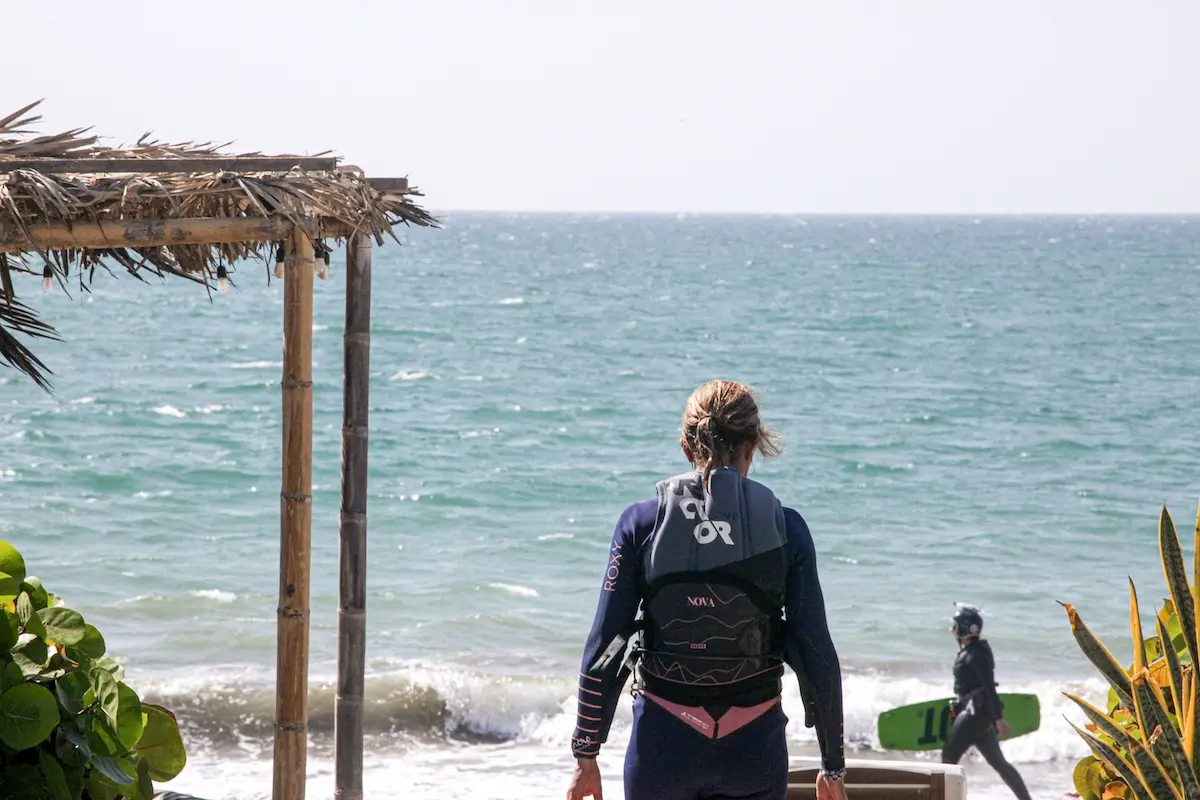 Woman in wetsuit and harness looking out at the ocean before kitesurfing at Kite Sisters women's camp Peru.