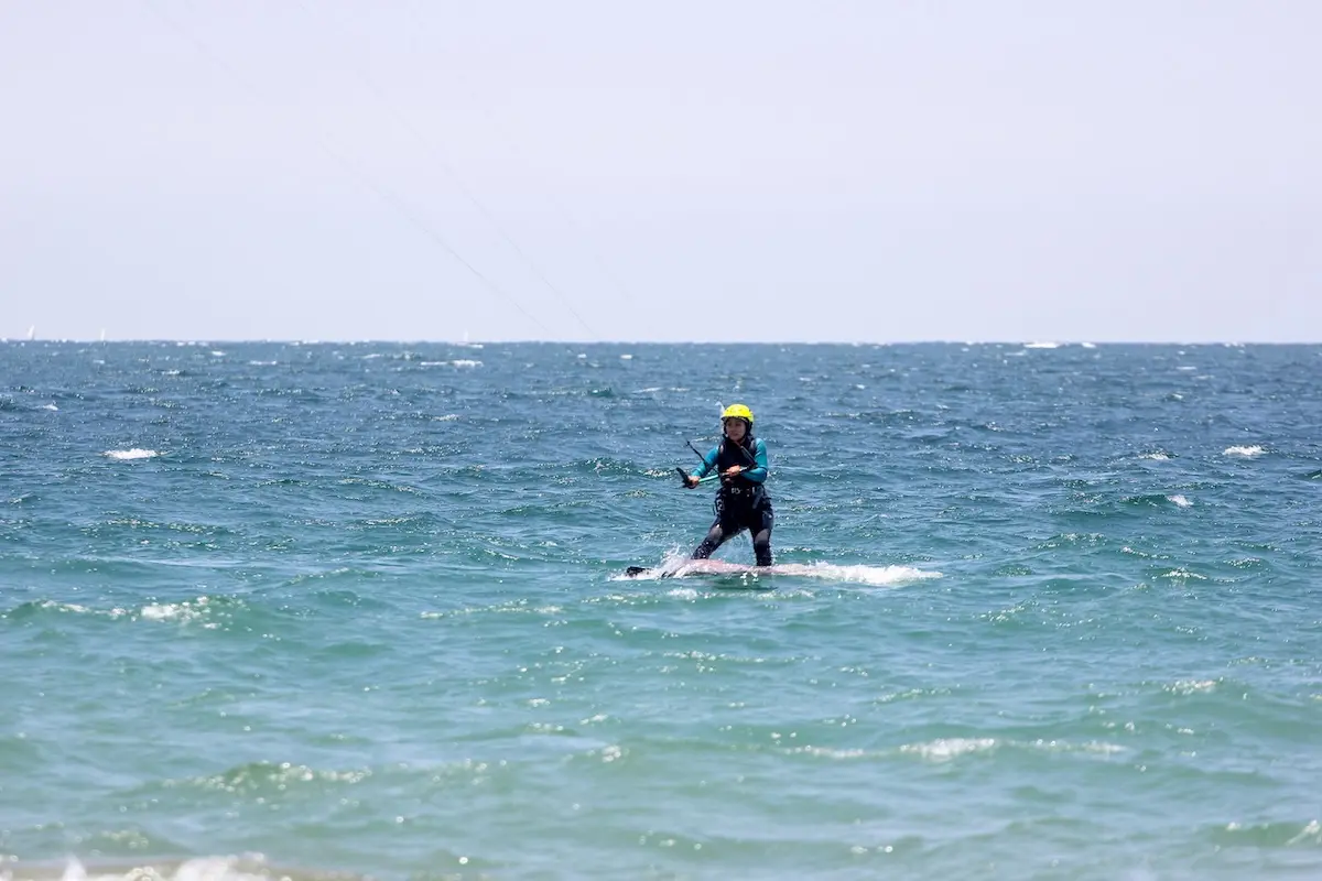 Woman in wetsuit and yellow helmet kitesurfing on turquoise ocean at Kite Sisters women's kiteboarding camp Peru.