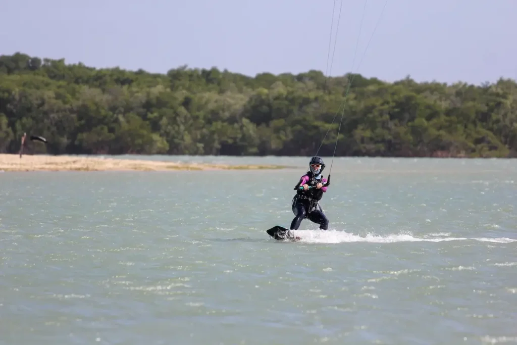 Woman learning Kiteboarding on a Lagoon – Kiteboarding Retreat Brazil - Kite Sisters Woman learning kiteboarding across a flat water lagoon surrounded by green mangroves during a kiteboarding retreat in Brazil.