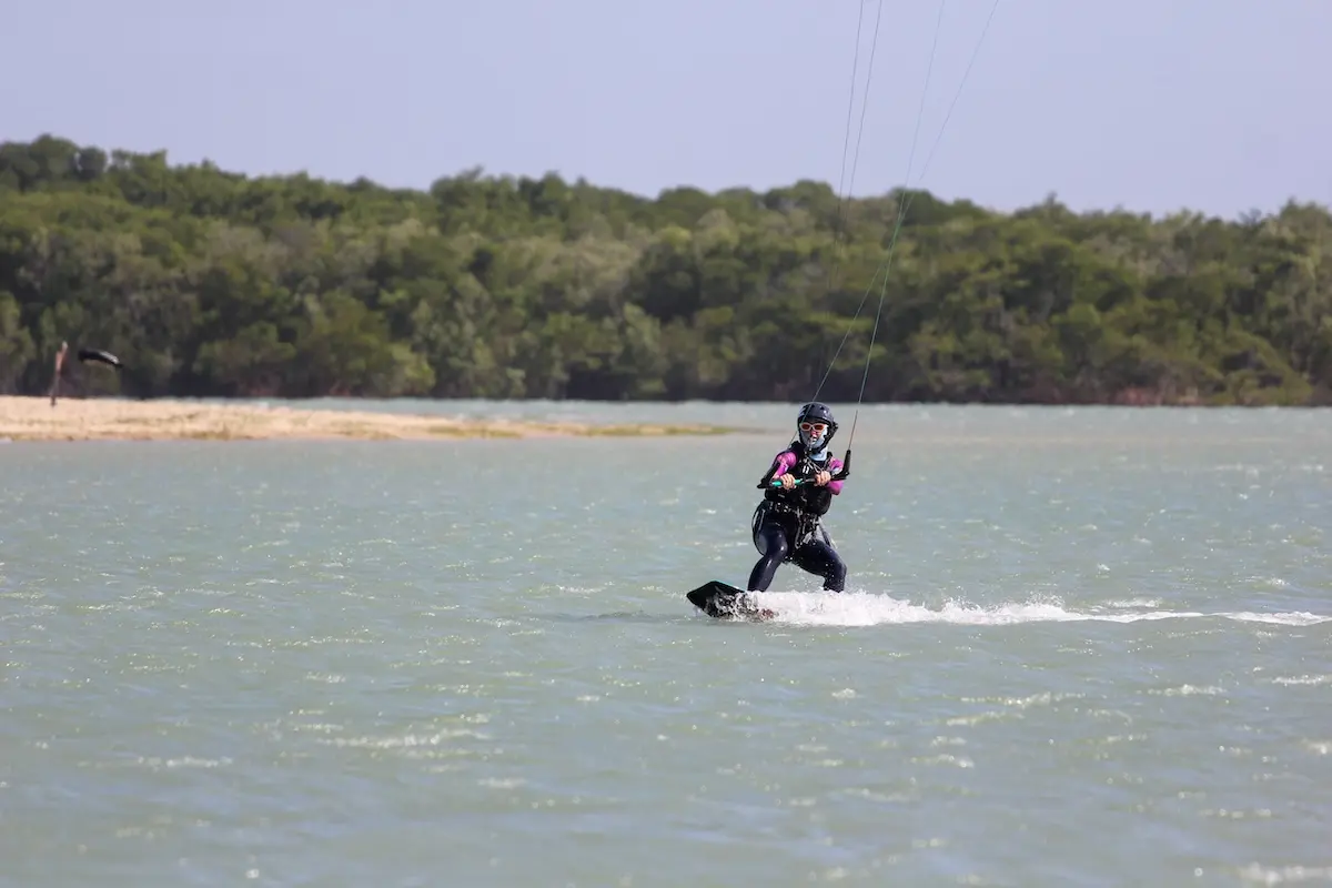 Woman learning kiteboarding across a flat water lagoon surrounded by green mangroves during a kiteboarding retreat in Brazil.