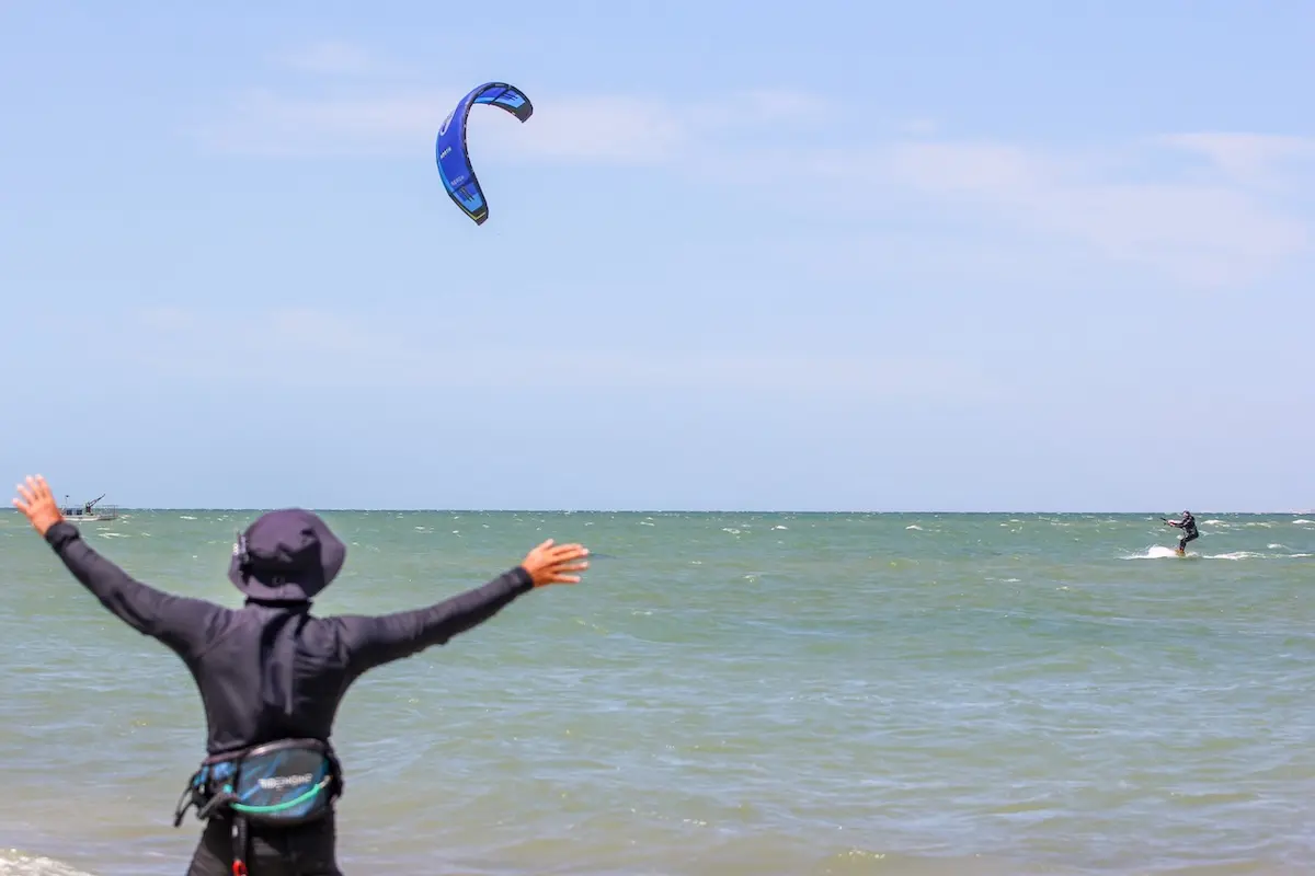 Instructor standing in the water with arms raised cheering as students kiteboards in the distance during a Morocco kiteboarding retreat.