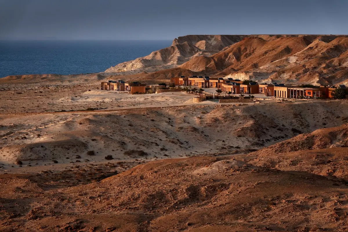 Wide landscape view of a boutique lodge nestled between red desert cliffs and the Atlantic Ocean at a Morocco kitesurf retreat in Dakhla.