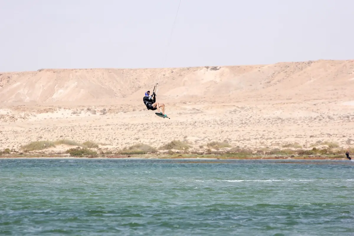 Kitesurfer performing a high jump over the turquoise lagoon with desert dunes in the background during a Morocco kitesurf retreat.