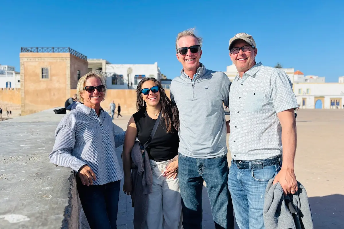 Group of four smiling kitesurf retreat clients posing in front of Essaouira's historic medina walls during a Morocco kitesurf retreat.