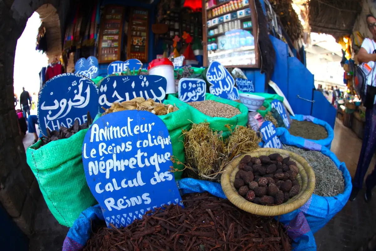 Vibrant Moroccan spice market stall with colorful burlap sacks and hand-painted blue signs in the Essaouira souk during a Morocco kitesurf retreat cultural excursion.