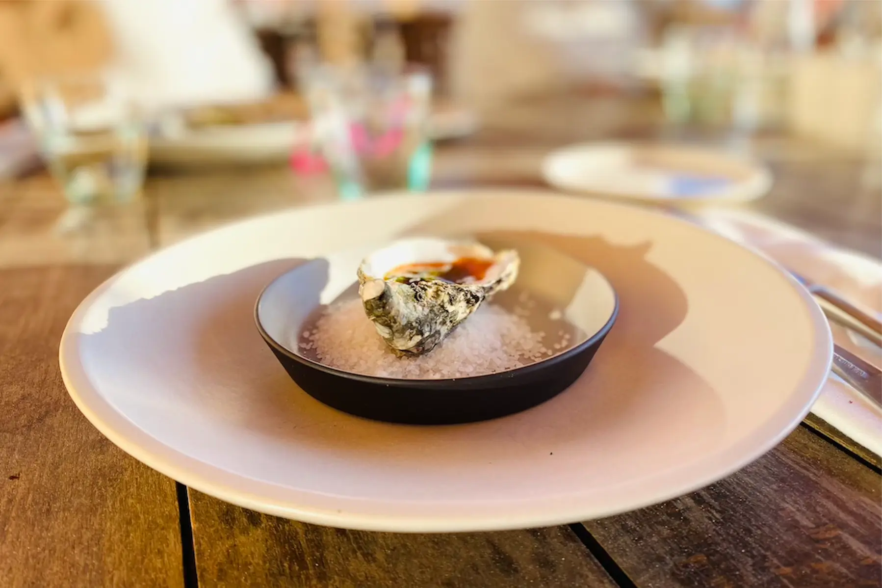 Single fresh oyster served on rock salt in a dark bowl on a white plate at a Morocco kitesurf retreat restaurant.
