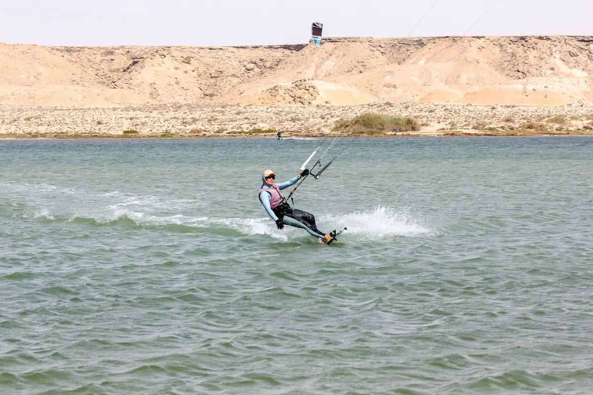 Woman kitesurfing across a flat water lagoon with arid desert hills in the background during a Morocco kitesurf retreat.