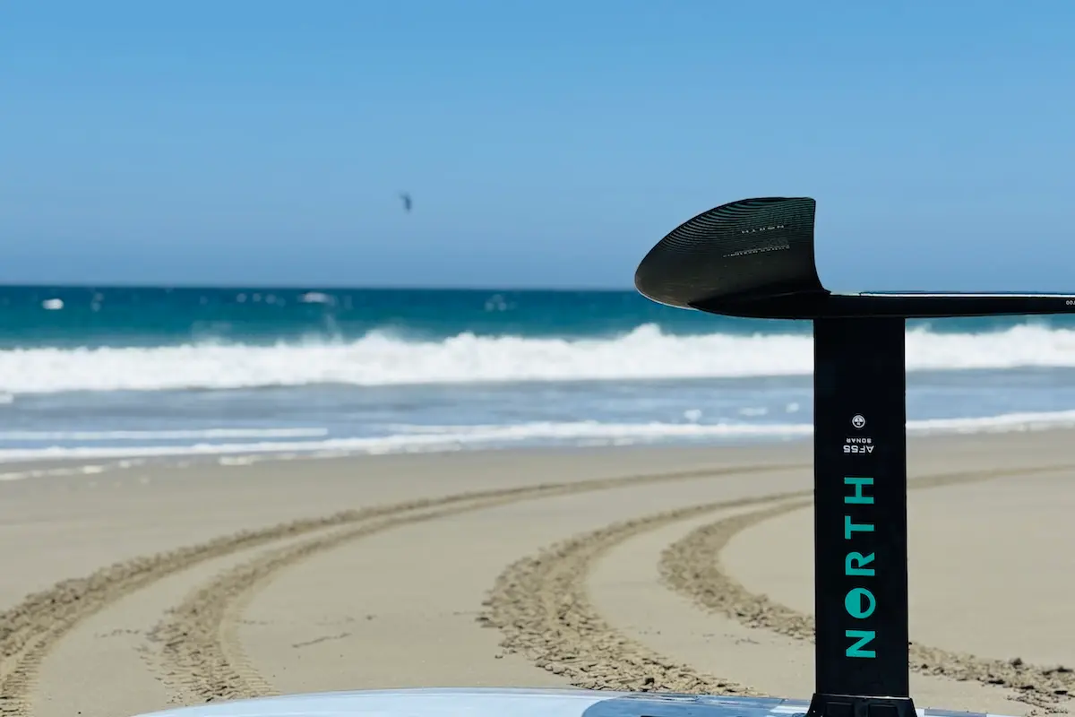 Close-up of a North foil mast and wing on a sandy beach with ocean waves in the background at a women's wingfoil camp in Peru.