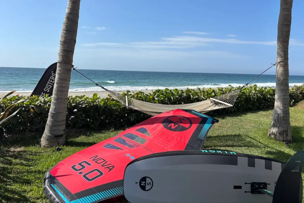 North Nova 5.0 wing and board resting on the grass between palm trees with a hammock and ocean view at a women's wingfoil camp in Peru.